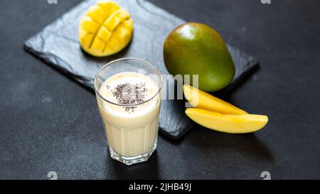 Kühler Mango-Milchshake auf schwarzem Hintergrund. Ein Getränk, um Ihren Durst im Sommer zu stillen. Indische Küche klassischer Drink - Lassi. Milch, Joghurt mit Mango Stockfoto
