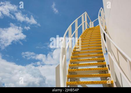 Große Industrietanks für Öl mit einem Gehweg auf und ab der Metalltreppe des Öltanks am blauen Himmel. Stockfoto