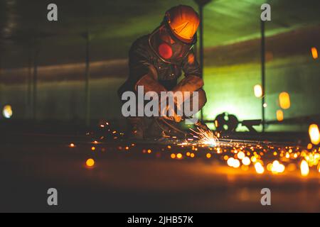 Metallspender des männlichen Arbeiters auf der Stahlplatte des Behälterbodens mit Blitzlicht in Nahaufnahme Schutzhandschuhe und Maske auf engem Raum tragen Stockfoto