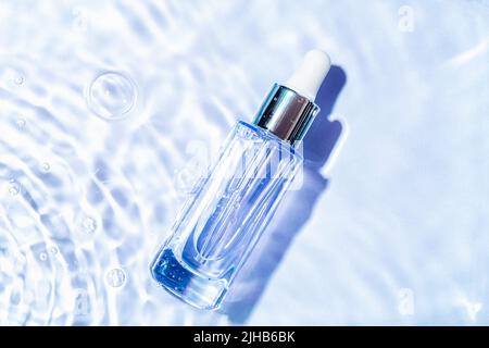 Glas-Serumflasche mit Kollagen auf blauem Wasserhintergrund mit Wasserblasen. Werbung für Medizinprodukte zur Anti-Aging-Pflege. Kosmetisches Spa medizinisch Stockfoto