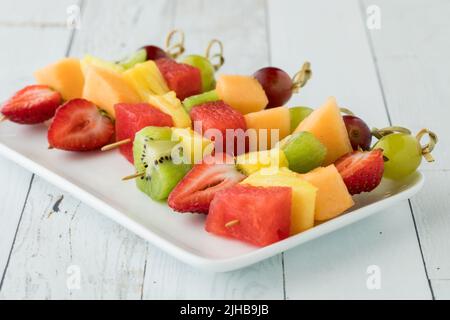 Fresh fruit kebabs on a small platter on a white wash wooden table. Stockfoto