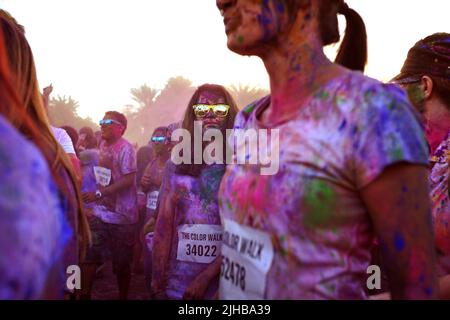 Die junge Frau, die voll mit farbigem Pulver bedeckt ist, posiert scherzhaft wie ein Zombie beim Color Walk, einem lustigen Sommerereignis im Freien in Dubai, Vereinigte Arabische Emirate. Stockfoto