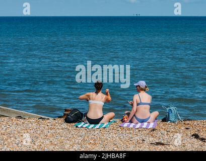 Zwei Frauen entspannen sich an einem heißen Sommertag an einem Kiesstrand in Whitstable, Kent, Großbritannien Stockfoto