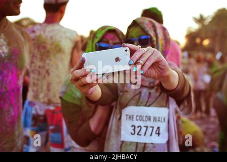 Zwei arabische Freunde, Frauen in Hijabs, machen beim Color Walk in Dubai, Vereinigte Arabische Emirate, ein mit farbigem Pulver bedecktes iPhone-Selfie Stockfoto