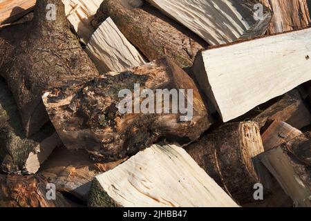 Nahaufnahme eines Stapels geschnittener Holzstämme, die mit einer Axt für Brennholz gespalten und zur Saison überlassen wurden Stockfoto