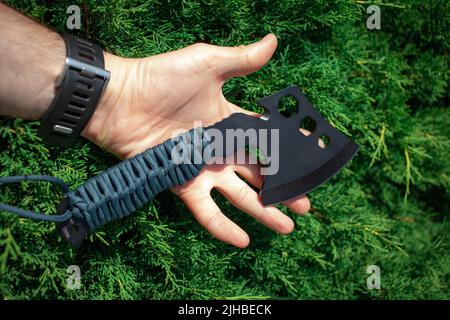 Eine kleine schwarze Axt mit einem Griff in Paracord-Verpackung. Ein Werkzeug zum Schneiden von Ästen oder Brennholz im Wald. Selbstverteidigungswaffe. Grüner Hintergrund. Stockfoto