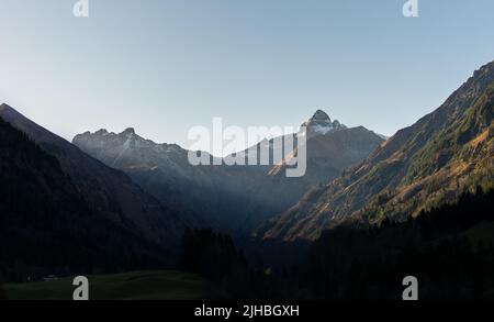 Bergtal mit Sonnenstrahlen, die bei dramatischem Sonnenaufgang durch die Berggipfel scheinen. Wunderschöne Naturlandschaft. Oberstdorf, Deutschland Stockfoto