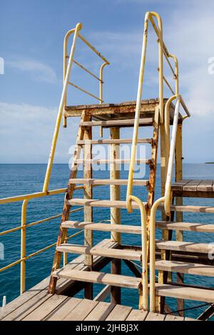 Schwimmbereich oder Pier am Meer. Ein großer Pier mit einem Dach, Holzbohlen und rostigen Treppen, die ins Wasser hinuntersteigen. Bade- und Ruheplatz. Stockfoto