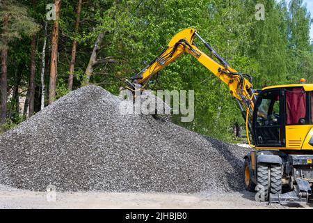 Der Bagger nimmt einen Eimer mit zerkleinerten Steinen aus einem großen Schutthaufen Stockfoto