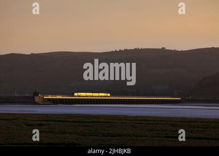 Network Rail Infrastructure überwacht den Zug, der das Arnside Viadukt auf der malerischen Bahnlinie der Cumbrian Coast überquert, mit einem goldenen Glanz bei Sonnenuntergang Stockfoto
