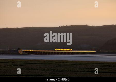 Network Rail Infrastructure überwacht den Zug, der das Arnside Viadukt auf der malerischen Bahnlinie der Cumbrian Coast überquert, mit einem goldenen Glanz bei Sonnenuntergang Stockfoto