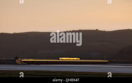 Network Rail Infrastructure überwacht den Zug, der das Arnside Viadukt auf der malerischen Bahnlinie der Cumbrian Coast überquert, mit einem goldenen Glanz bei Sonnenuntergang Stockfoto