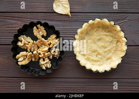 Nüsse tart Zubereitungen, Teig und Nüsse auf braunem Holztisch, Draufsicht. Herbstgelbe Blätter. Stockfoto