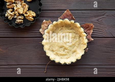 Nüsse Tortenzubereitungen, Teig und Nüsse auf braunem Holztisch, Draufsicht. Herbstlaub Dekoration. Stockfoto
