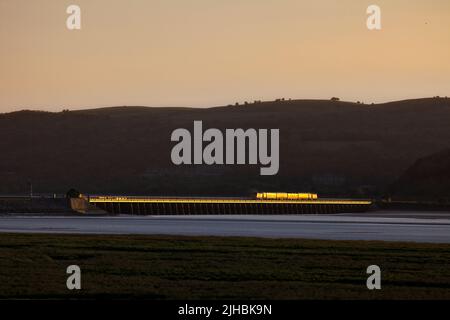 Network Rail Infrastructure überwacht den Zug, der das Arnside Viadukt auf der malerischen Bahnlinie der Cumbrian Coast überquert, mit einem goldenen Glanz bei Sonnenuntergang Stockfoto