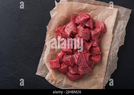 Rohes, gehacktes Rindfleisch. Rohes Bio-Fleisch vom Rind oder Lamm, Gewürze, Kräuter auf altem Pergamentpapier auf dunkelgrauem Betongrund. Gulasch. Roh hat mich nicht angekocht Stockfoto