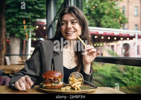 Attraktive junge Frau, die in einem Restaurant Pommes und einen Burger isst. Stockfoto