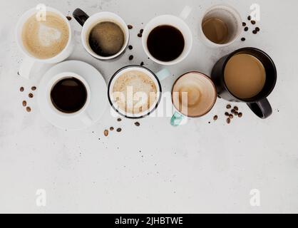 Draufsicht auf flachem Lay mit vielen verschiedenen vollen und leeren Kaffeetassen Zusammensetzung auf grauweißem Beton Hintergrund. Layout mit verschiedenen Teetassen. Getrocknete Kaffeebohnen. Espresso, Latte, Americano Stockfoto