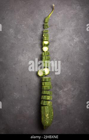 Frisch angewinkelte Luffa in Scheiben geschnitten auf einem schwarzen strukturierten Hintergrund, auch bekannt als gerippter Kürbis oder chinesische Okra, gesundes Gemüse von oben genommen Stockfoto