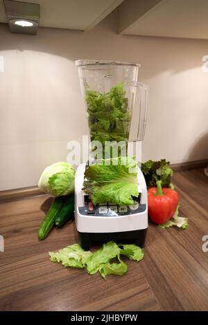 Einen grünen Smoothie, Salat in einem Mixer mit Gemüse auf der Arbeitsplatte einer Küche, das Konzept eines gesunden Lebensstils Stockfoto