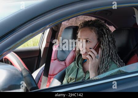 Porträt einer attraktiven asiatischen Frau mittleren Alters, die in einem offenen Autofenster telefoniert. Stockfoto