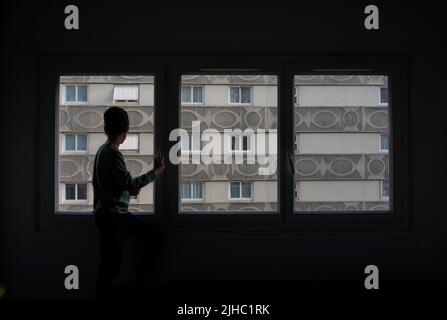 Das Kind blickt aus dem Fenster der Wohnung. Sozialer Wohnungsbau (HLM), flaches Wohngebäude, 4 rue de Crimée, 75019, Paris, Frankreich Stockfoto