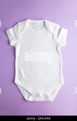 Nachbau von einfacher Baumwollkleidung für Babys. Weißer Body für Mädchen und Jungen auf violettem Hintergrund. Nahaufnahme. Flaches Layout für das Design und das Platzkonzept Stockfoto