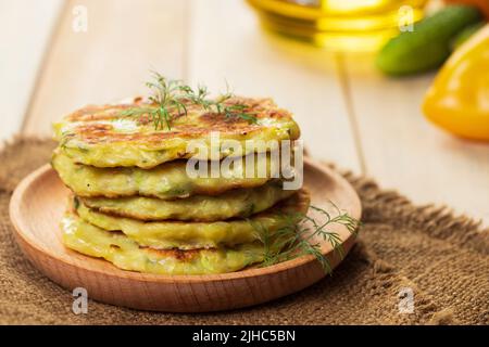 Stapel grüner Zucchini-Pfannkuchen auf Holzplatte. Gesunde vegane Ernährung Nahaufnahme. Vegetarische Krapfen auf Leinenservietten. Stockfoto