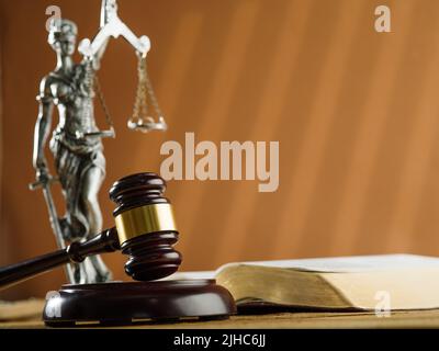 Nahaufnahme. Ein hölzerner Gavel eines Richters, eine Bronzeguine der Göttin der Gerechtigkeit - Themis und ein offenes Buch auf beigem Hintergrund. Die Rechtsstaatlichkeit. Jud Stockfoto