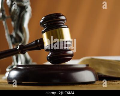 Traditionelle Symbole eines fairen amerikanischen Gerichts - ein Richtergavel, eine Statue von Themis und ein offenes Buch auf beigefarbenem Hintergrund. Nahaufnahme. Rechtsstaatlichkeit, Recht, Stockfoto