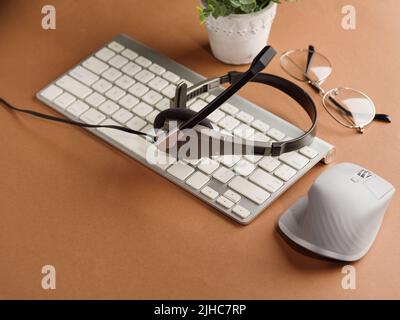 Komfortabler Ort für Arbeit und Erholung. Moderne Geräte - Kopfhörer, Computertastatur, Maus, Brille und Dekor - Innenblume auf beigefarbenem Hintergrund. W Stockfoto