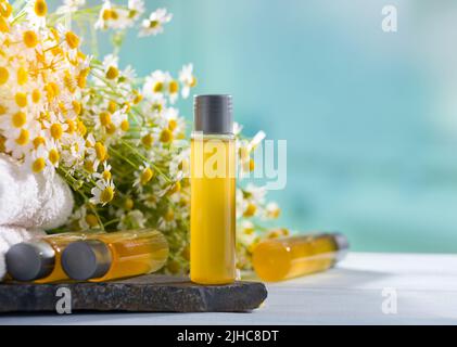 Kamille-Aromatherapie. Flaschen mit ätherischem Öl, Handtüchern und frischen Kamillenblüten. Kräuteröle für Spa und Schönheit Stockfoto