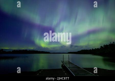 Nordlichter brechen über einem See in Minnesota im dunklen Himmel über dem Himmel aus und strahlen einen Regenbogen aus Licht und Farben Stockfoto