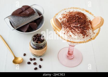 Einfache und schnelle hausgemachte Tiramisu für einen unerwarteten Besuch, süß keine Backen Käsekuchen Stil Dessert mit Zutaten auf weißen Holztisch platziert. Hoher Angl Stockfoto