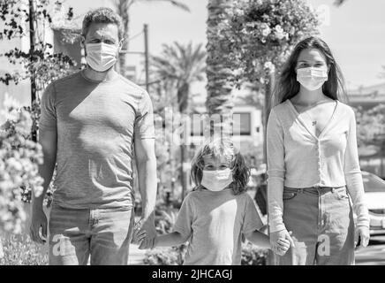 Junge Familie von Mutter Vater und Sohn tragen Schutzmaske zu Fuß im Freien, covid Stockfoto