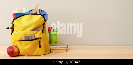 Schulrucksack mit Papeterie und Apfel auf Tisch vor hellem Hintergrund Stockfoto