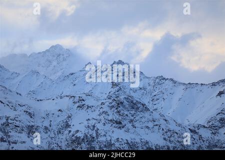 Die schneebedeckten Berge Alaskas berühren die vorbeiziehenden Wolken am kalten Winterhimmel Stockfoto