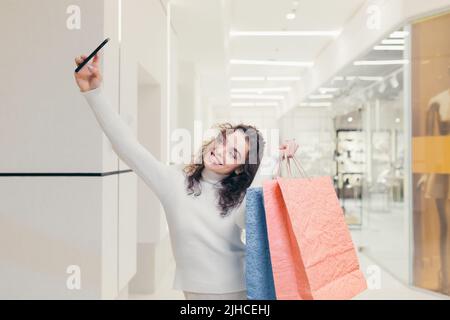 Junge, schöne Frau kauft im Geschäft ein und spricht bei einem Videoanruf mit Freunden. Bietet Shopping, Shows Shopping Stockfoto