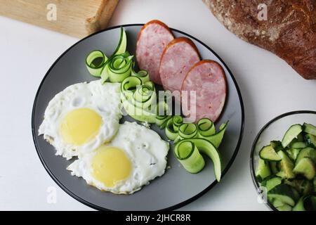 Zastrak-Eier Rühreier Wurst Salat Gurken auf der Trael Blick von der Seite oben. Traditionelles englisches amerikanisches Frühstück. Erste Mahlzeit. Das Benef Stockfoto