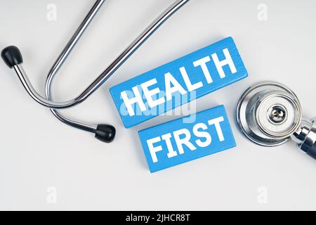 Medizin und Gesundheitskonzept. Auf dem Tisch ist ein Stethoskop und blauer Jenga mit der Aufschrift - GESUNDHEIT ZUERST Stockfoto