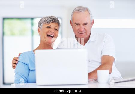 Fröhliches Paar mit Laptop. Fröhliches reifes Paar, das lächelt, während es zu Hause einen Laptop benutzt. Stockfoto