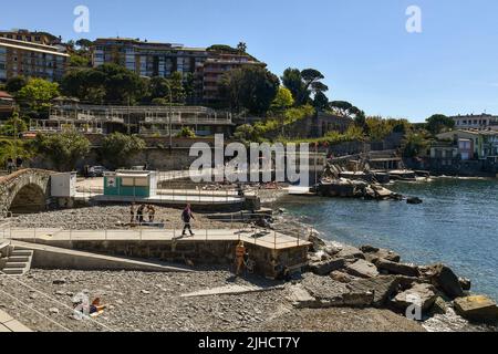 Blick auf die Promenade mit Menschen Sonnenbaden am Kiesstrand an einem sonnigen Frühlingstag, Rapallo, Genua, Ligurien, Italien Stockfoto