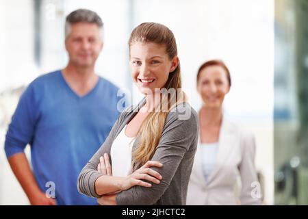 Begierig darauf, die Karriereleiter zu erklimmen. Eine attraktive junge Geschäftsfrau, die selbstbewusst mit ihren Mitarbeitern im Hintergrund steht. Stockfoto