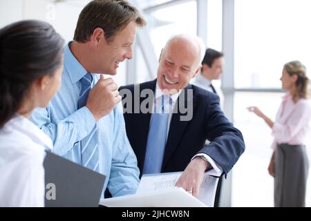 Dieser Bericht sieht fantastisch aus. Positive Geschäftsleute, die in einem informellen Treffen gemeinsam Dokumente durchgehen. Stockfoto