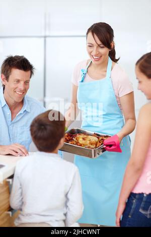 Es ist Ihre Lieblingsmahlzeit, mein Junge. Eine wunderschöne Mutter, die ihrer aufgeregten und hungrigen Familie einen perfekt gekochten Braten präsentiert. Stockfoto