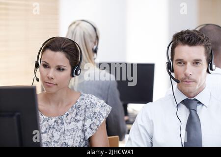 Konzentriert und freundlich. Zwei Kundendienstmitarbeiter, die im Hintergrund mit Kollegen zusammenarbeiten. Stockfoto