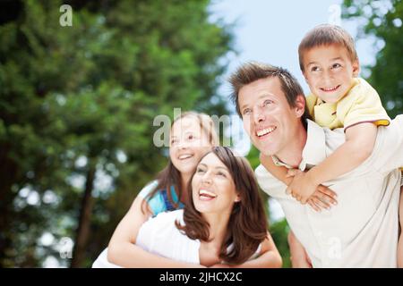 Eine wunderbare Familie, die einen Tag zusammen genießt. Low-View einer glücklichen und hingebungsvollen Mutter und Vater tragen ihre Kinder auf dem Rücken - Copyspace. Stockfoto