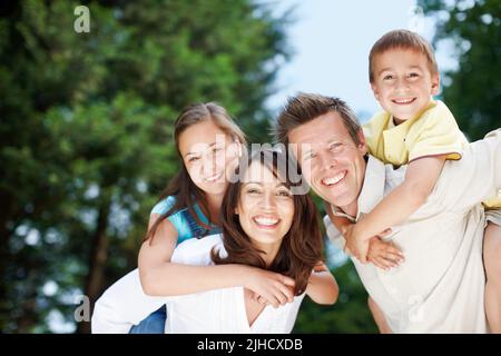 Familienausflüge machen immer den größten Spaß. Low-View einer glücklichen und hingebungsvollen Mutter und Vater tragen ihre Kinder auf dem Rücken - Copyspace. Stockfoto