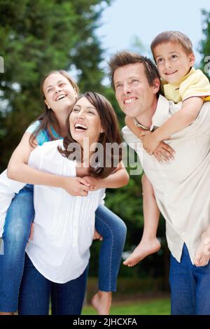 Die Zukunft unserer Familie ist finanziell gesichert. Low-View einer glücklichen und hingebungsvollen Mutter und Vater tragen ihre Kinder auf dem Rücken - Copyspace. Stockfoto