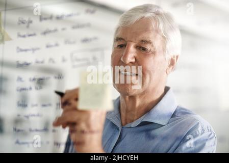 Ohne Planung kann man kein großer Geschäftsmann sein. Ein leitender Geschäftsmann schreibt Ideen mit einem Stift-Marker auf eine Glaswand im Büro. Stockfoto